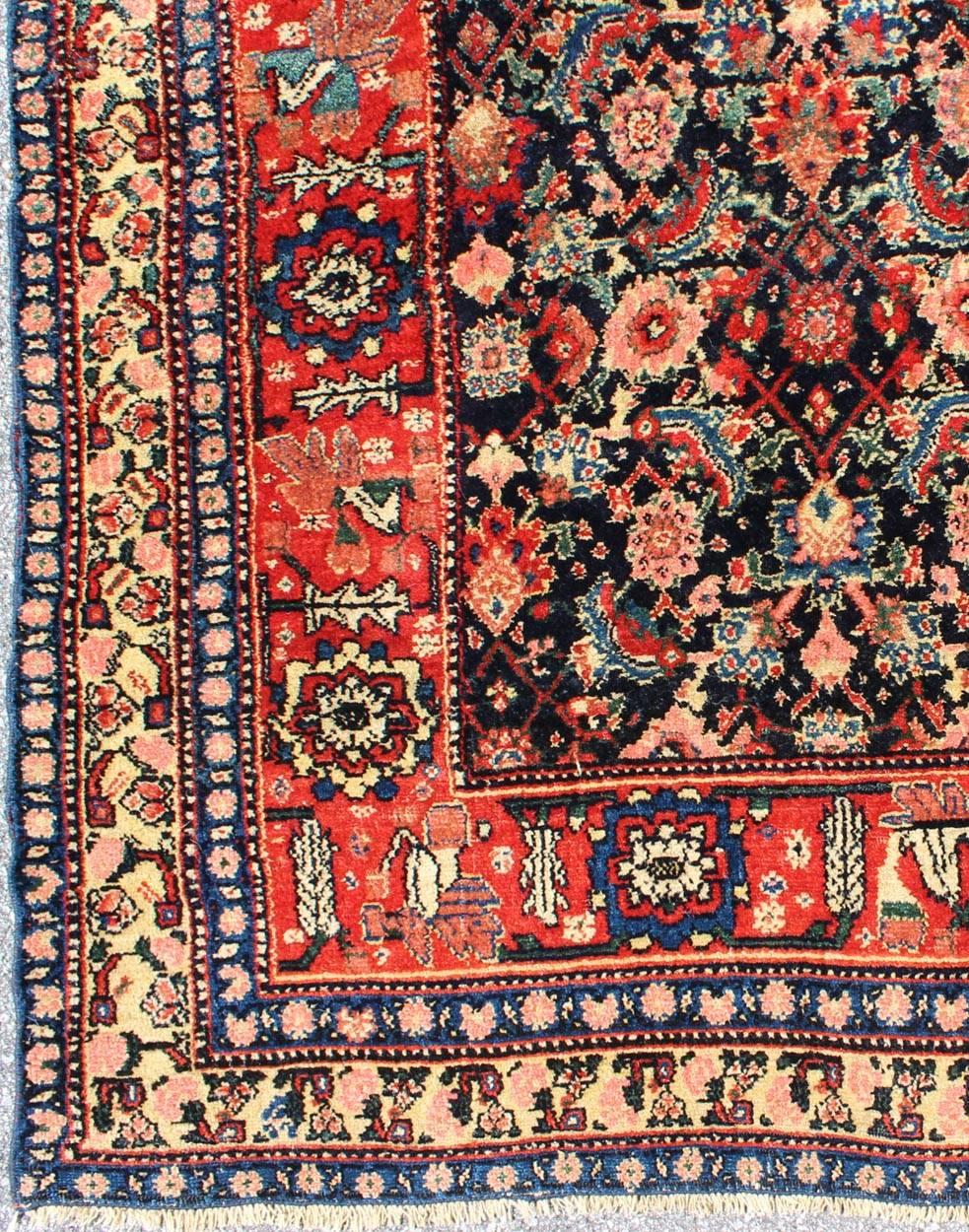This piece is a Northwest Persian Bidjar carpet with a navy field decorated by red lattice-work and various flowers in shades of coral, sky blue, green, light camel, mahogany, ivory and red. Ivory and sky blue speckling appears in some of the