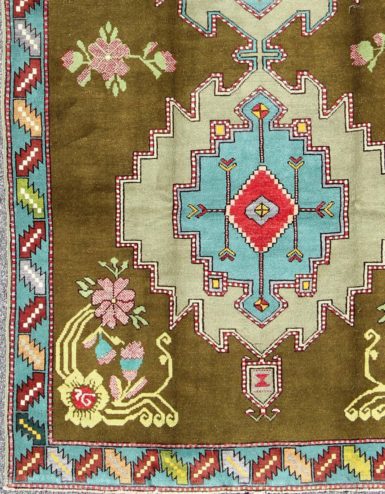 Measures: 5'10 x 9'8.
This lovely and unique Turkish carpet displays multi-layered geometric medallions. The unique colors of this piece include yellow, blue, red, teal, pink, bright yellow, salmon and many green shades of Green, including tones of