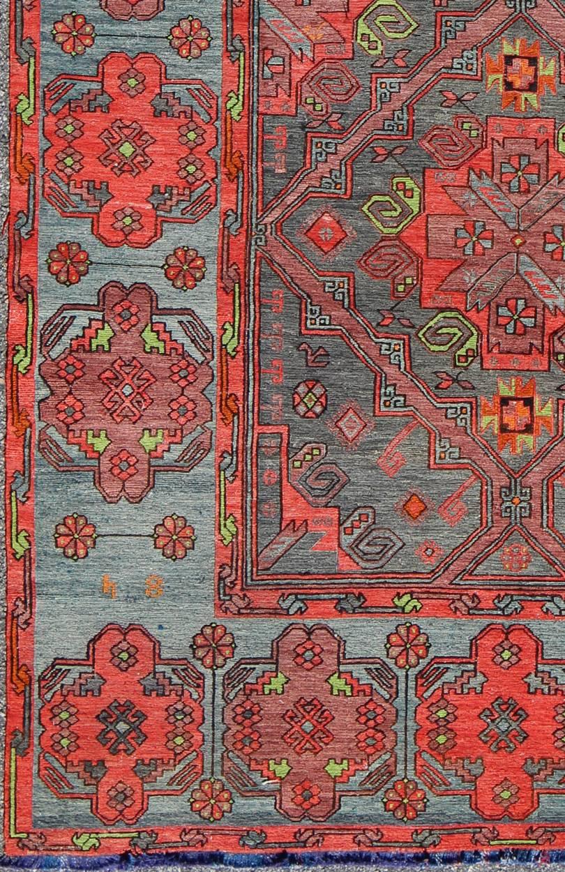 This vintage Caucasian Sumak features large-scale diamond medallions on charcoal field with vibrant red and green. A set of ornate medallions decorate the wide border on a beautiful blue/gray background. Curated from an exclusive selection, these