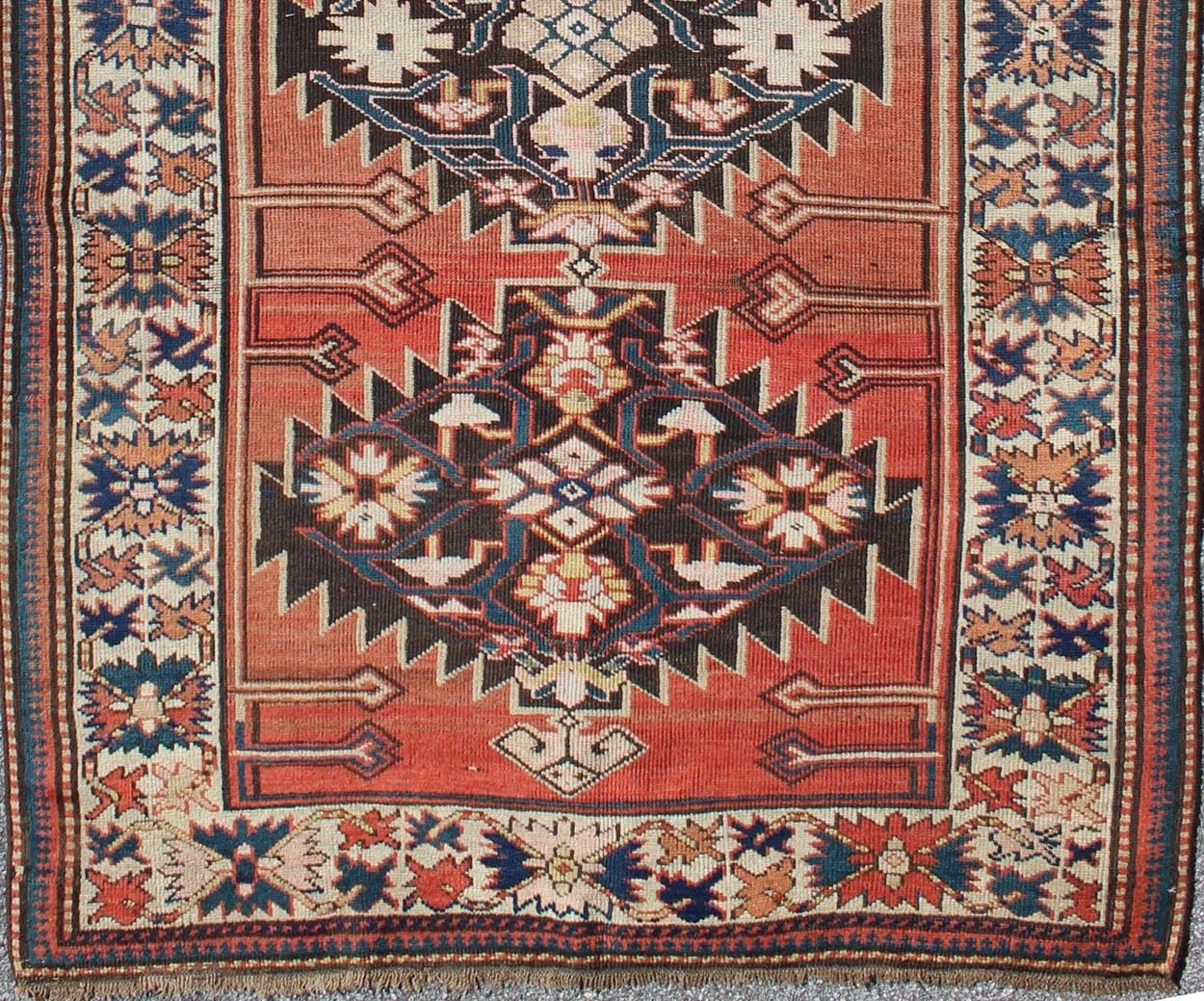An antique southwest Caucasian Kazak rug with four complete latch hook or animal head style medallions, on an abrashed terracotta color field. Three borders in shades of navy blue, ivory and mid blue frame the filed. 
Measures: 4'3 x 8'10.
List