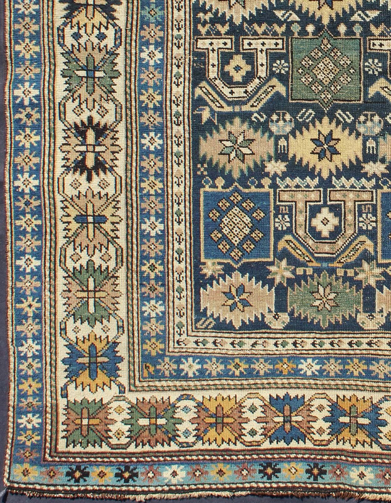 Measures: 3'3'' x 4'5''.

The field of this Caucasian piece features all-over tribal motifs and shapes decorated with small flowers and square designs, alternating colors between tan, blue, green and yellow. A blue background cradles the motifs with