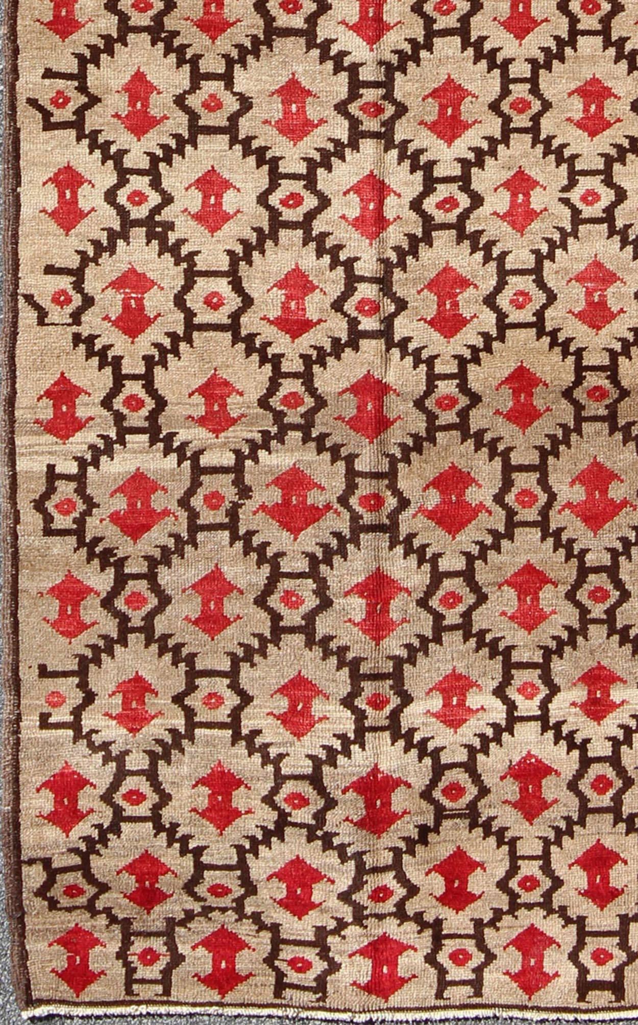 This unique Turkish carpet features an all-over geometric and tribal design set on a camel field and complemented by shades of brown and red. 
Measures: 4'4 x 10'10.