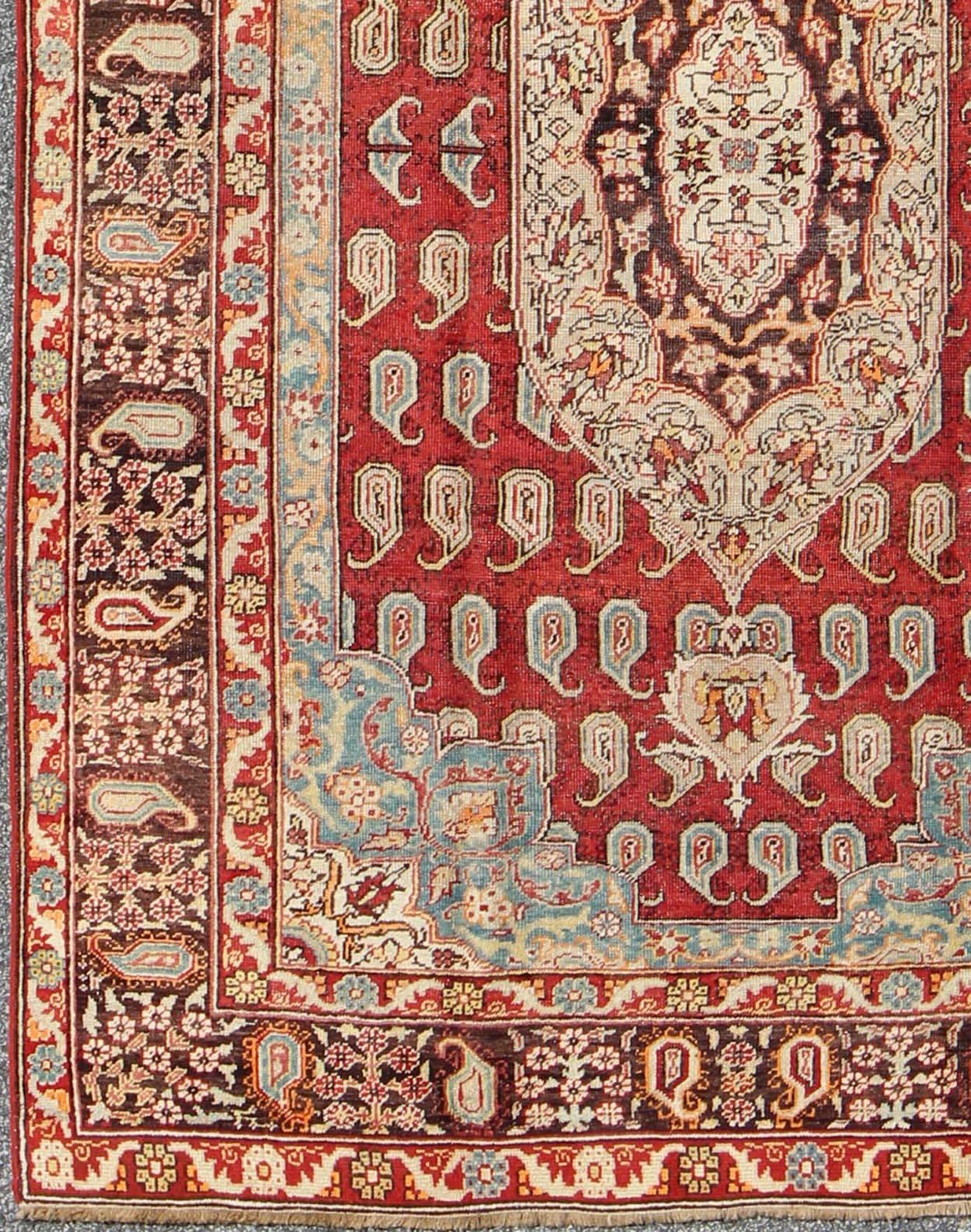 Antique Turkish Oushak Rug with Paisley Design in Red, Brown and Blue.
This antique Turkish Oushak was beautifully handcrafted during the early part of the 20th Century. A regal sub-geometric design and center medallion rests upon a field of red. An