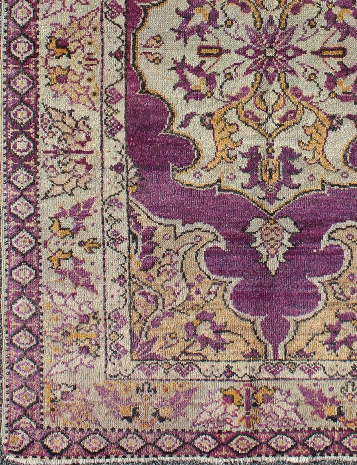 Measures: 3'6'' x 5'8''.
This lovely vintage Oushak is set on a purple background and features a floral medallion with accents of deep gold. The taupe border has a unique flower pattern with accent colors of the field while the small diamond outer