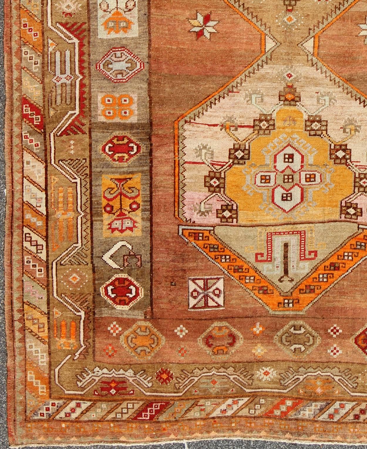 This beautiful Turkish Oushak rug, handwoven in Turkey, features an exquisite geometric design with two large medallions. The medium tone colors include an earthy palette with pops of orange, blue, pink, green, red camel, yellow and coral. An ornate