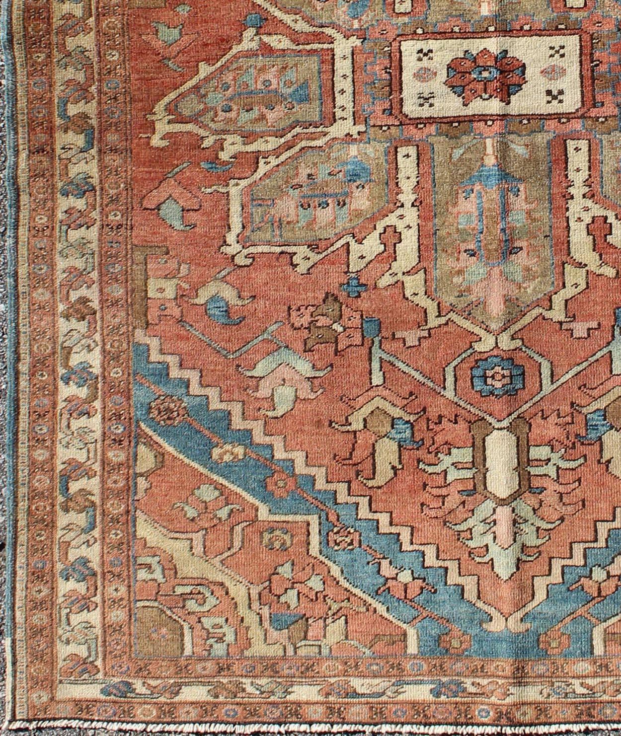 This lovely antique Persian Serapi rug was woven in the early 20th Century and bears a large, blossoming, geometric central medallion and an overall geometric floral design. The pale tomato red field holds the eight-point palmette-inspired
