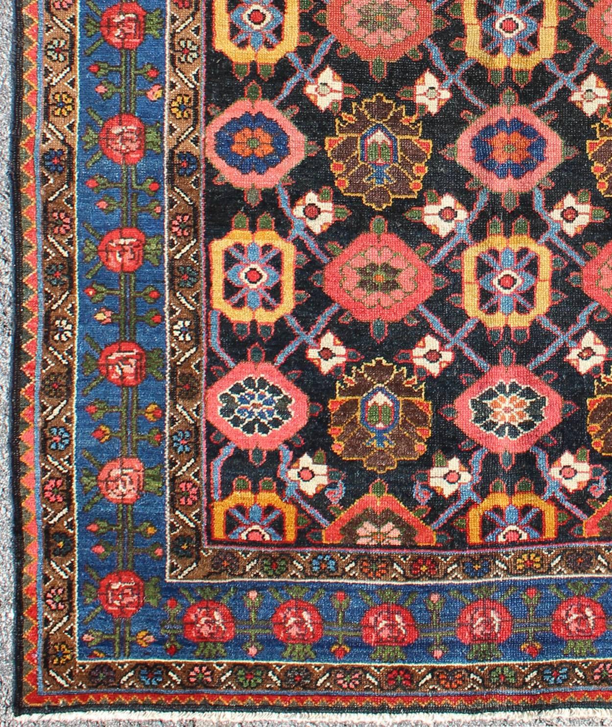 Cet ancien tapis persan Bakhtiar présente un motif floral sur toute sa surface dans des couleurs vives de rose, jaune, corail, orange, bleu et des touches d'ivoire. La bordure bleue est composée de fleurs roses et corail avec des vignes vertes. Les