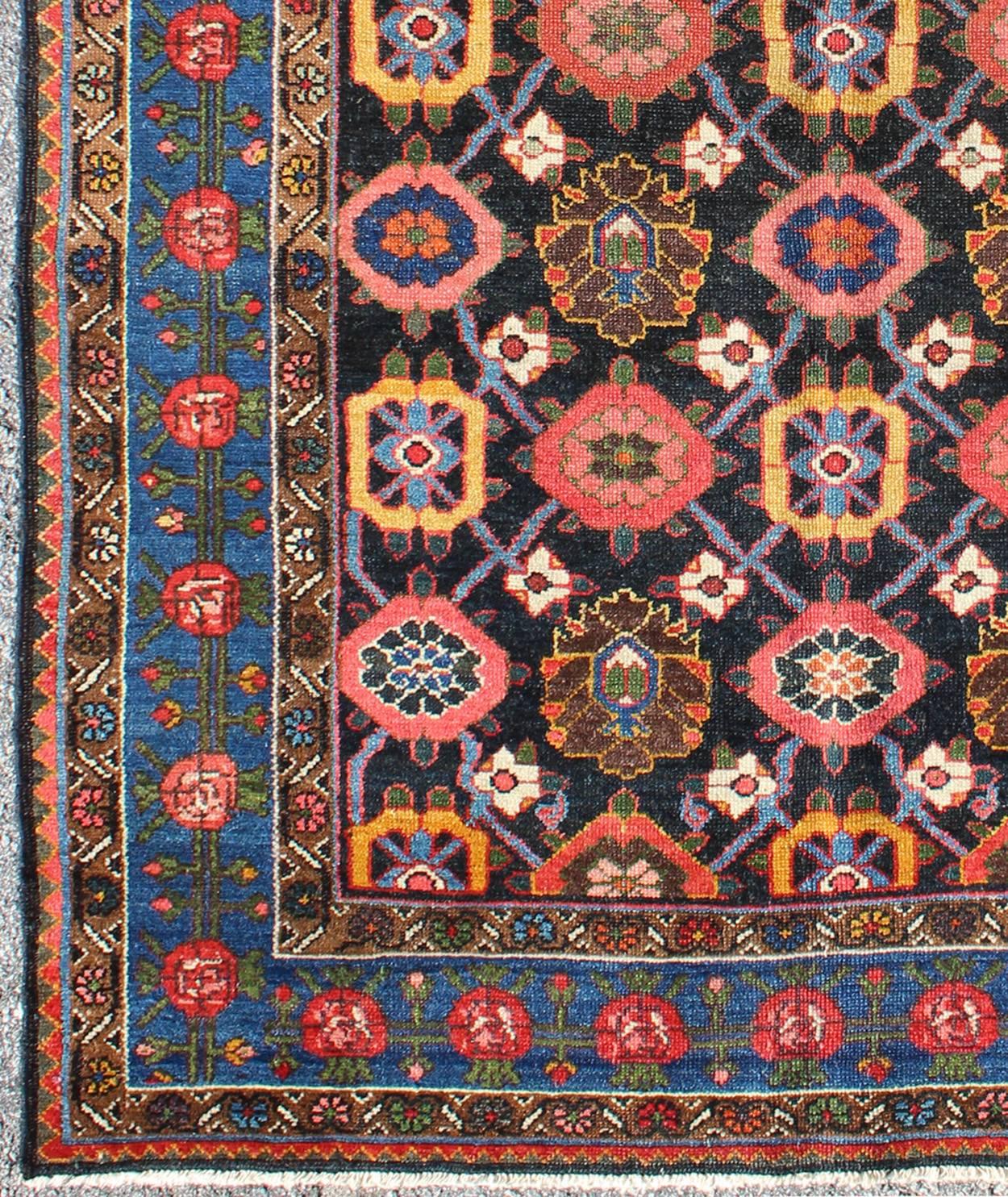Dieser antike persische Bakhtiar-Teppich zeigt ein florales Muster in leuchtenden Farben wie Rosa, Gelb, Koralle, Orange, Blau und einem Hauch von Elfenbein. Die blaue Umrandung besteht aus rosa und korallenroten Blumen mit grünen Ranken. Der