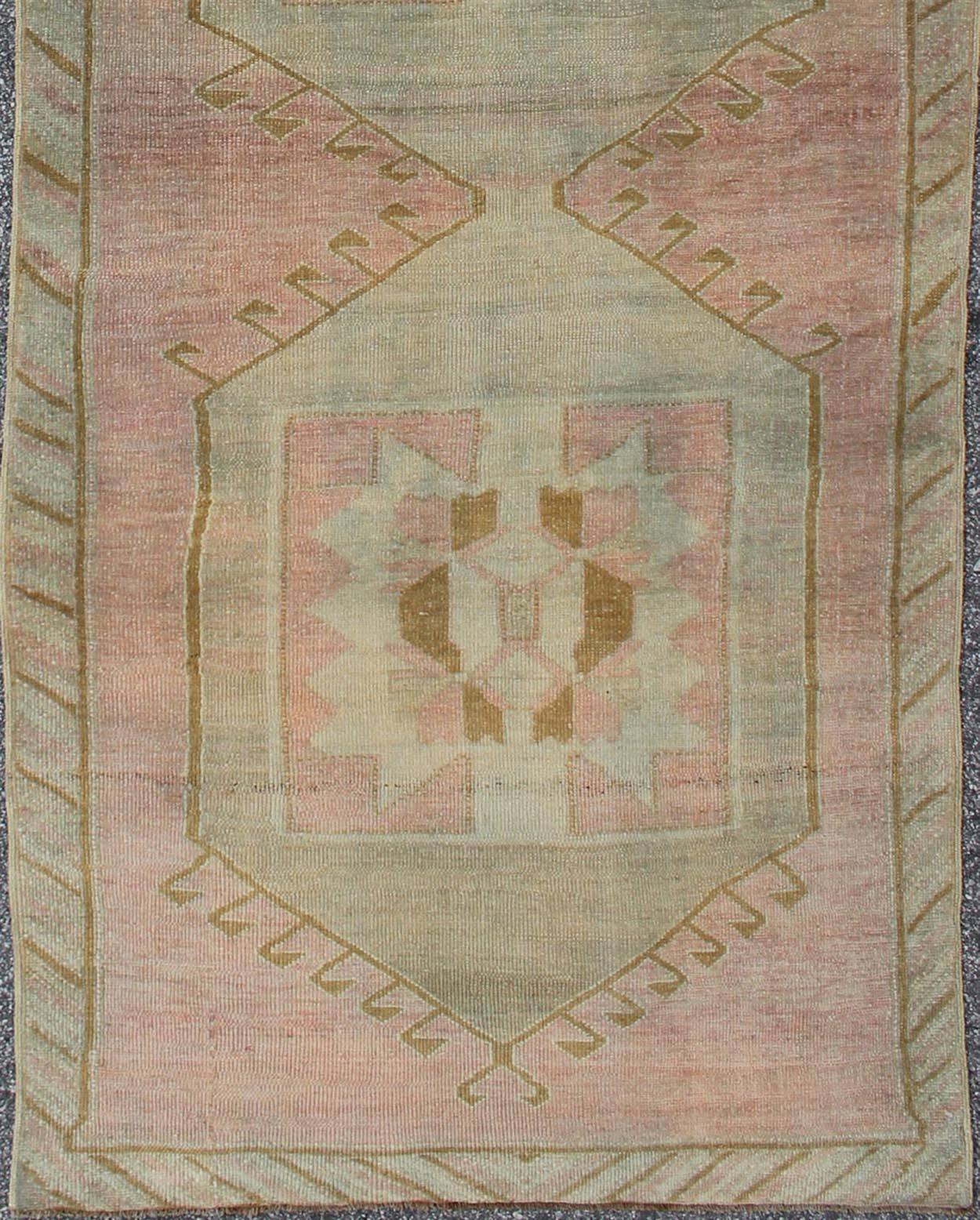 This unique Oushak runner features a geometric pattern inspired by tribal design. The unique tribal motifs, coupled with pink and light blue hues, culminate in a highly decorative and richly intricate piece. 
Measures: 3'8 x 11'6.