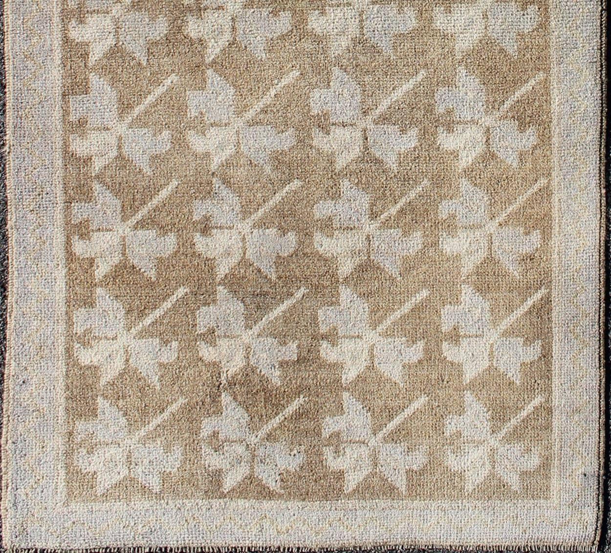 Set on a camel and brown background and accented by neutral cream and light blue, this tribal Turkish Oushak rug showcases five geometric patterns that stretch throughout the entire field of the rug. A multi-tiered border with repeating geometric