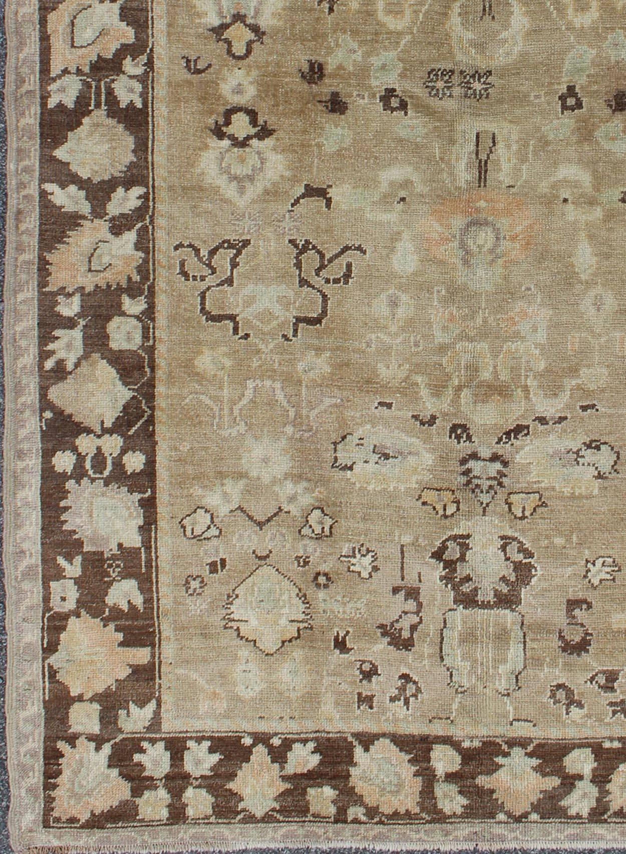 This wonderful vintage Turkish Oushak from the mid-20th century features a taupe background and a chocolate-brown border. The flowers in the border are rendered in cream, light blue, and peach-coral. The field pattern features cream, muted yellow,