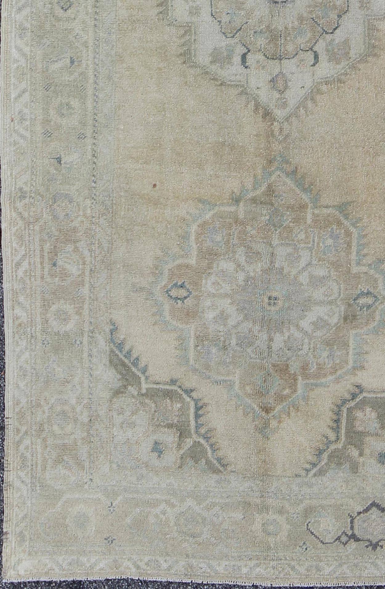 This vintage Oushak beautifully illustrates the impressive craftsmanship and design of Turkish weavers. The large botanical medallions flow through the centre field of taupe, light blue and ivory hues. Linear branches on either side of the