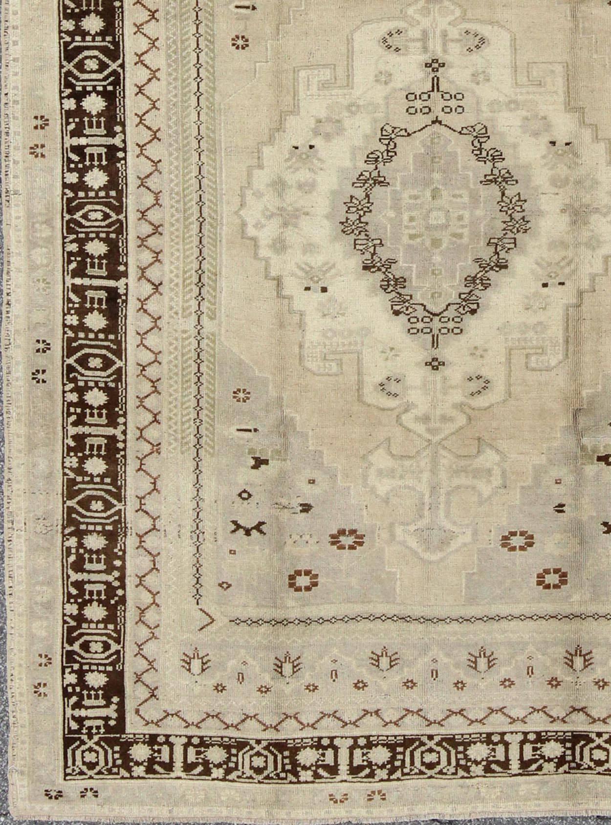 This vintage Turkish Oushak features a rich chocolate border and complementary outlines set on a taupe and cream background.  
Measures: 6'5 x 8'7.