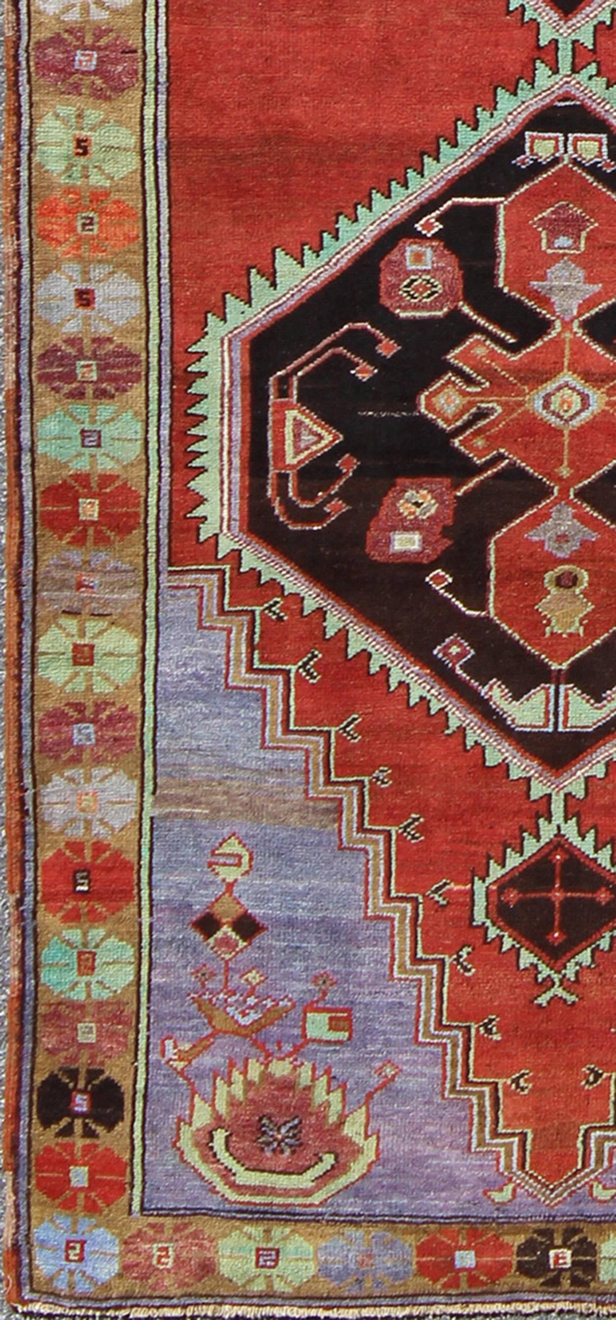 This beautiful vintage Oushak runner from mid-20th century Turkey is enhanced by its color palette and lustrous wool. The bright red ground is home to three large multi-layered medallions in red, green, grey, camel and charcoal. The medallions are