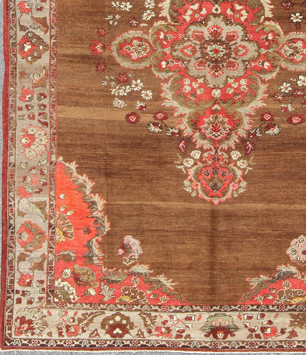 This very unique carpet, from eastern Turkey, displays a brown background with a gray/taupe border. The orange corners add vibrancy to the rug while the softer colors, such as taupe, gray, pale green and cream, calm the vibrant and bold nature of
