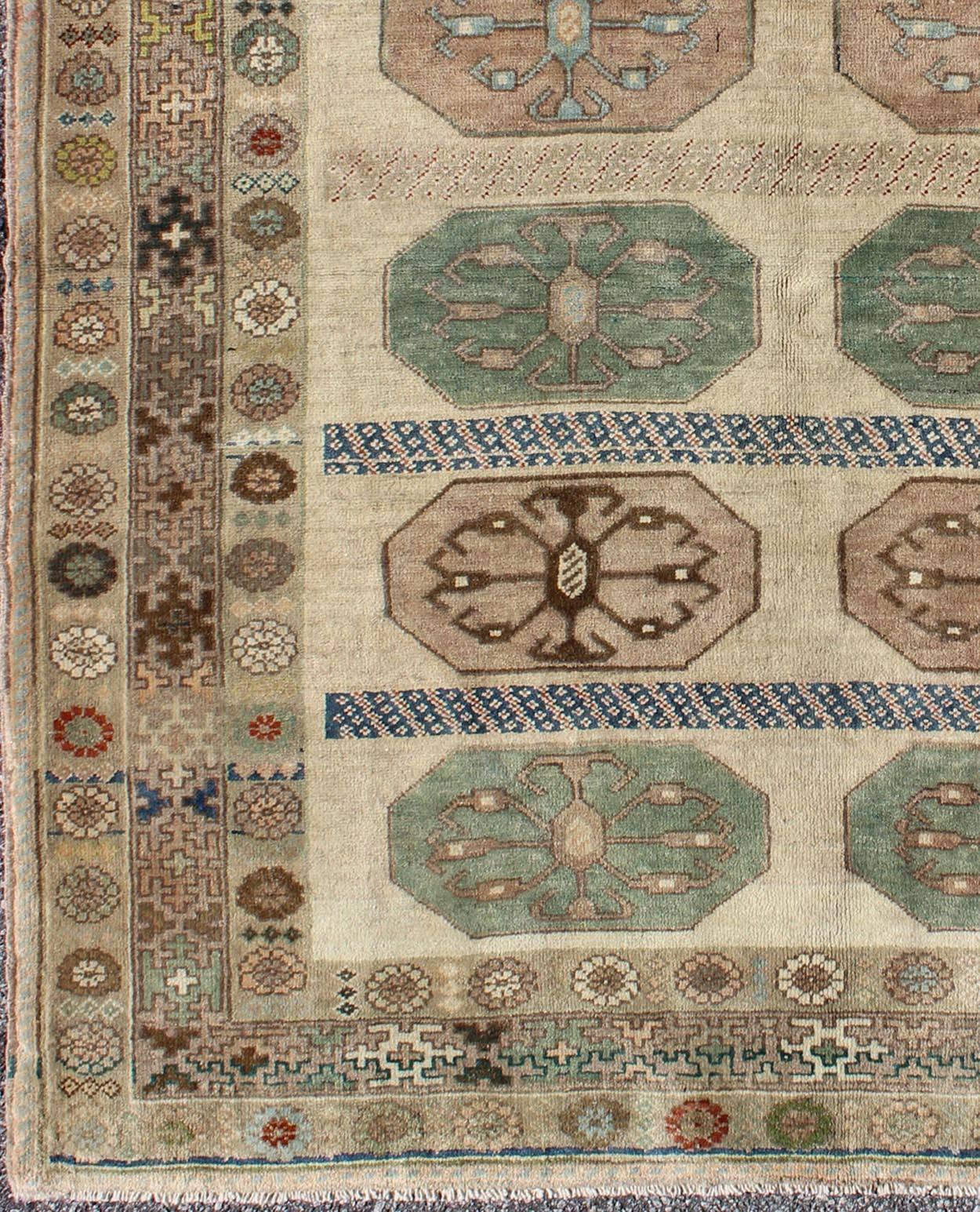 This vintage Turkish Oushak rug (circa mid-20th century) features a unique blend of colors and an intricately beautiful design. The central medallions are arranged in horizontal lines and consist of geometric-tribal designs. The various shades of