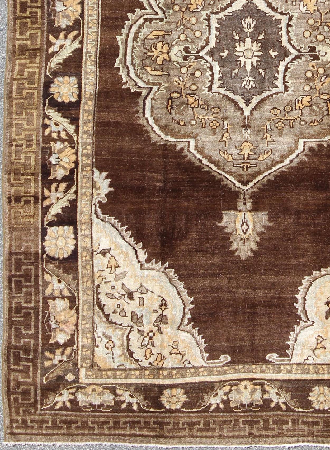This vintage Turkish Oushak rug, (circa mid-20th century) features a unique blend of colors and an intricately beautiful design. The ornate central medallion is complemented by a symmetrical set of floral motifs in the surrounding cornices and