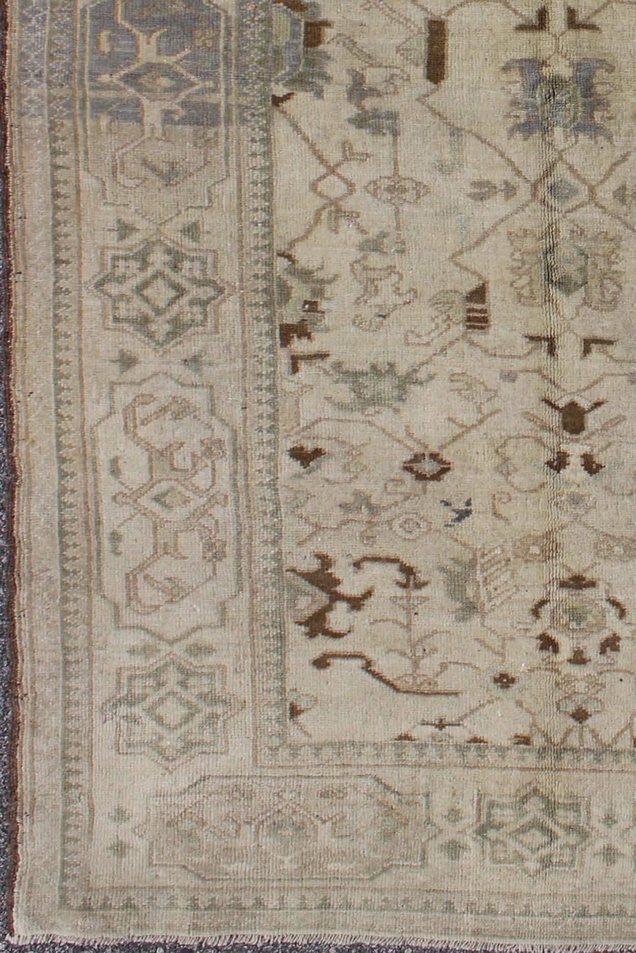 This vintage Turkish Oushak carpet (circa mid-20th century) features an all-over design of sub-geometric and tribal motifs. The rug's qualities are enhanced by its particularly soft and lustrous wool. Colors include ivory, gray, and brown, with