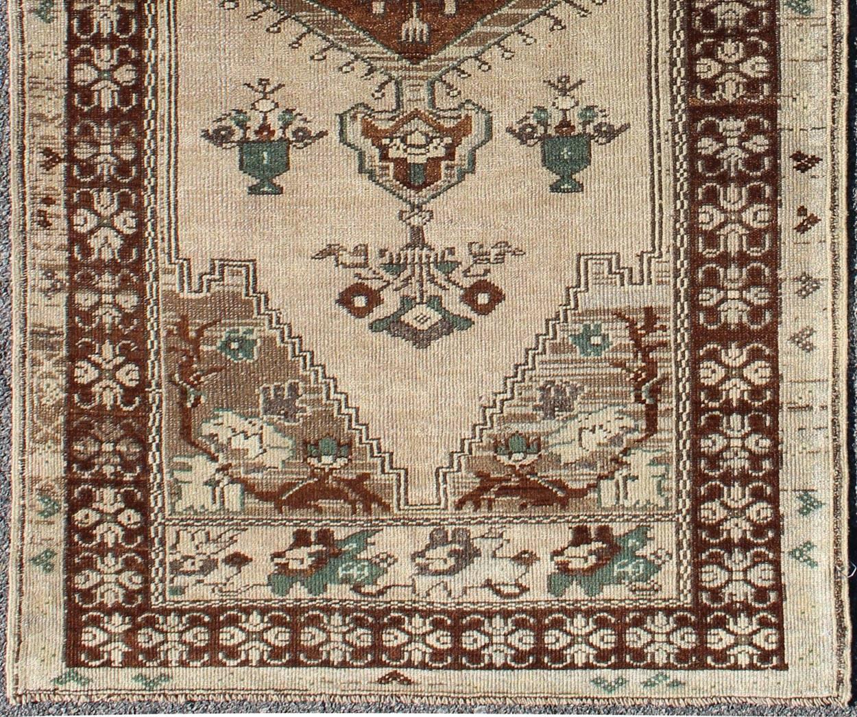 This vintage Turkish Oushak carpet (circa mid-20th century) features a central medallion design, as well as patterns of smaller flowers and floral elements in the four cornices, and in the surrounding borders. The rug's qualities are enhanced by its