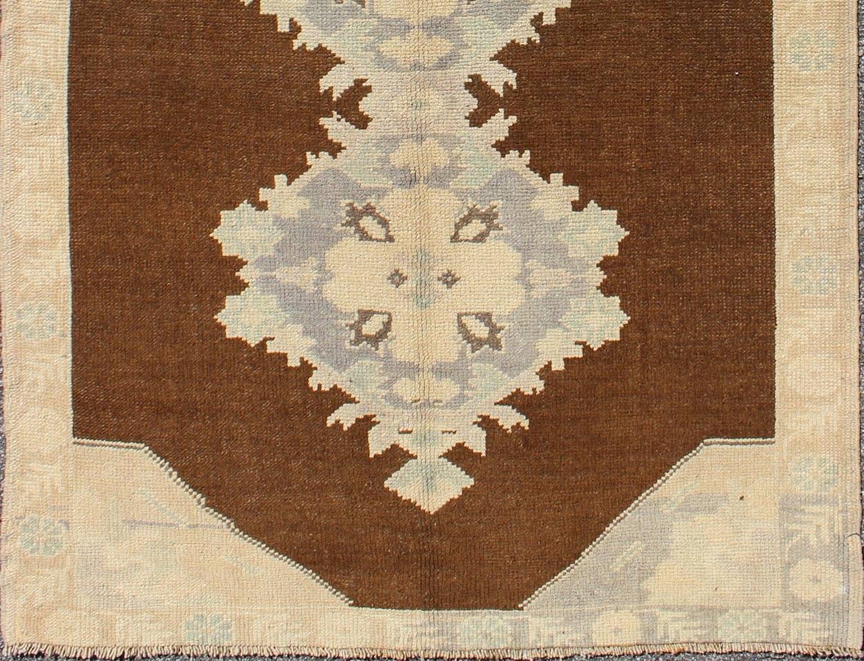 This vintage Turkish Oushak gallery rug (circa mid-20th century) features a unique blend of colors and an intricately beautiful design. The central medallions consist of a vertical line of floral elements, surrounded by faint complementary figures