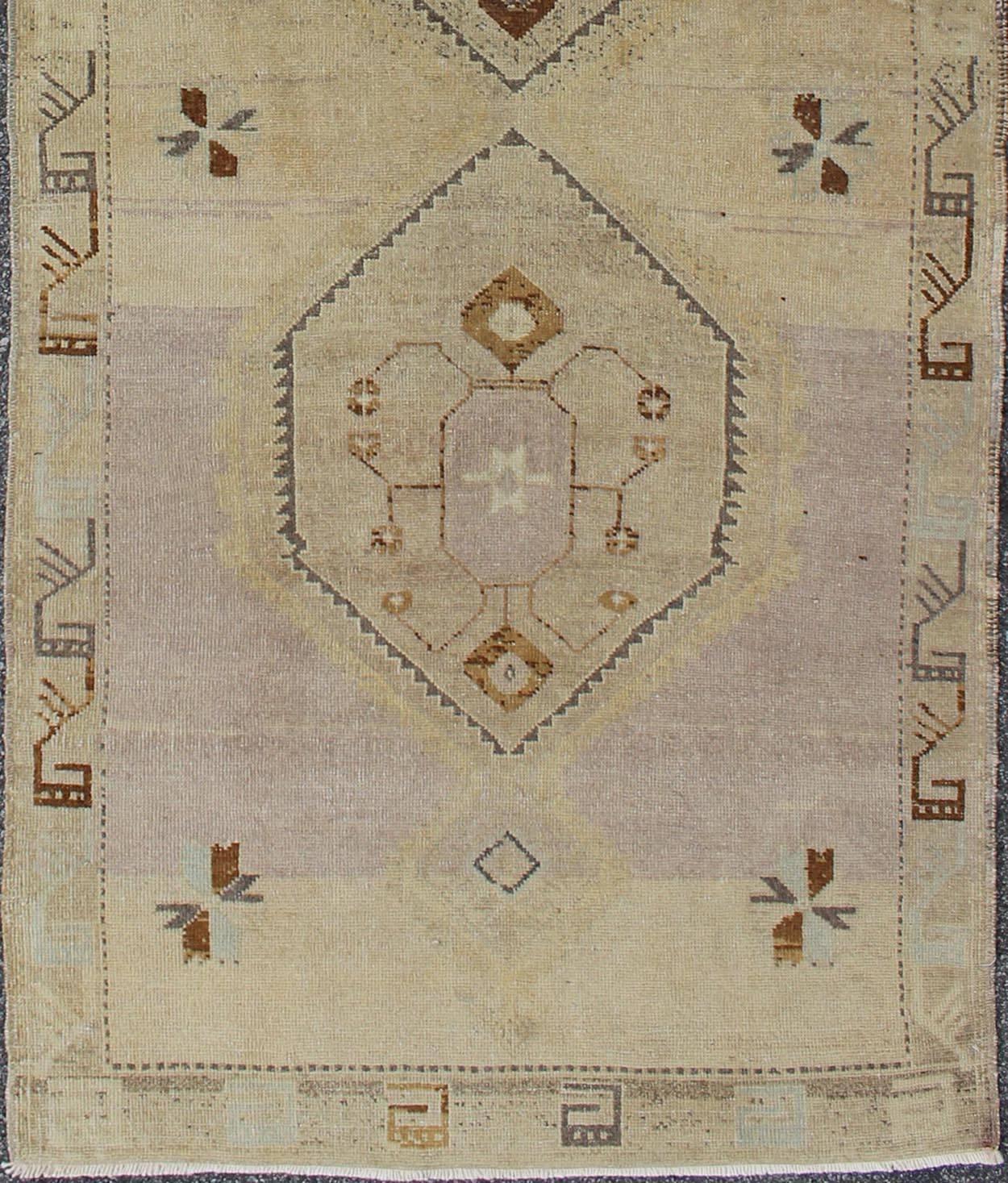 This vintage Turkish Oushak gallery rug (circa mid-20th century) features a unique blend of colors and an intricately beautiful design. The central medallions consist of a vertical line of tribal elements, surrounded by complementary figures in the