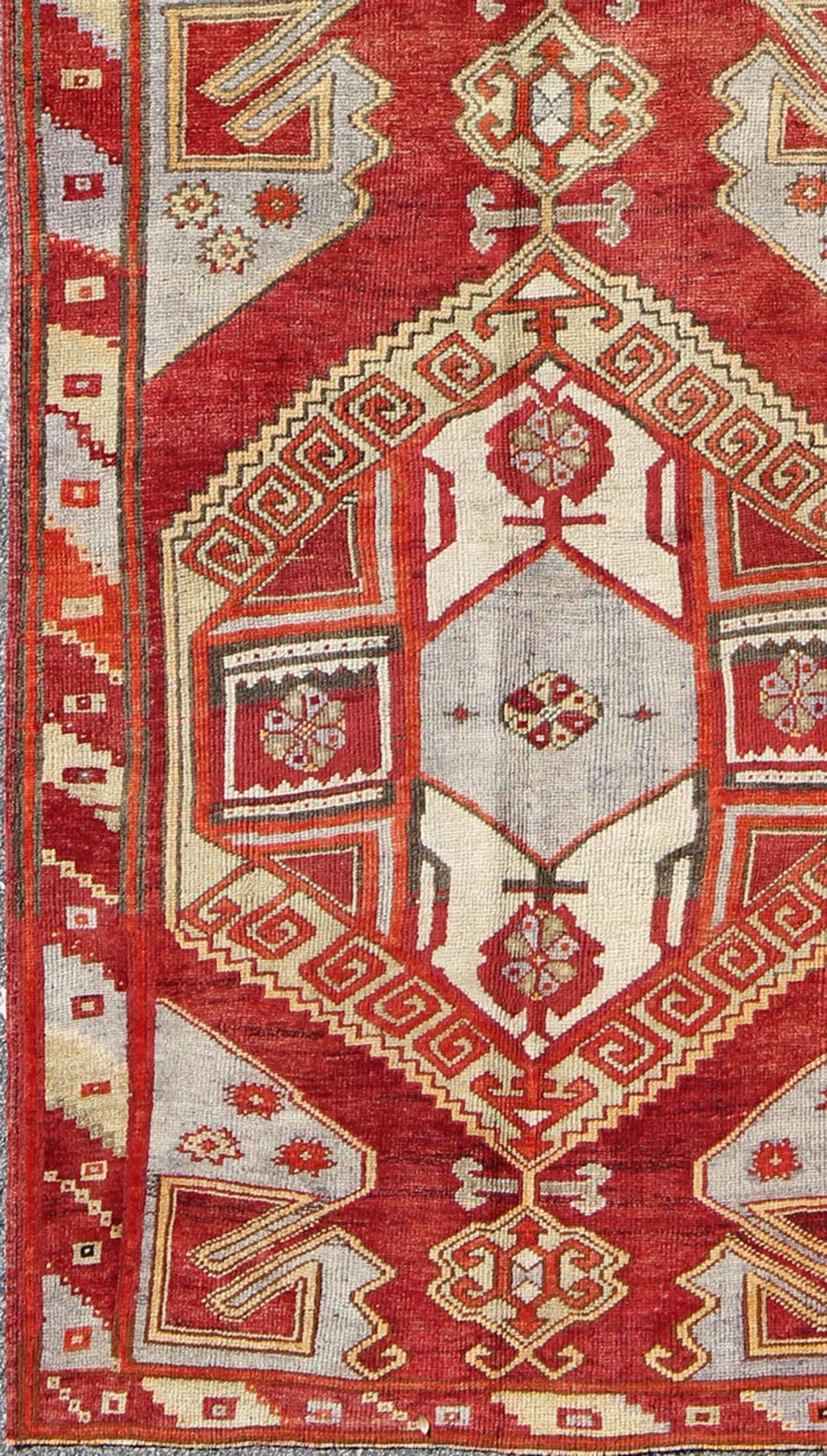 This vintage Turkish Oushak carpet (circa mid-20th century) features a central dual-medallion design, as well as patterns of geometric elements in the four cornices, and in the surrounding borders. The rug's qualities are enhanced by its