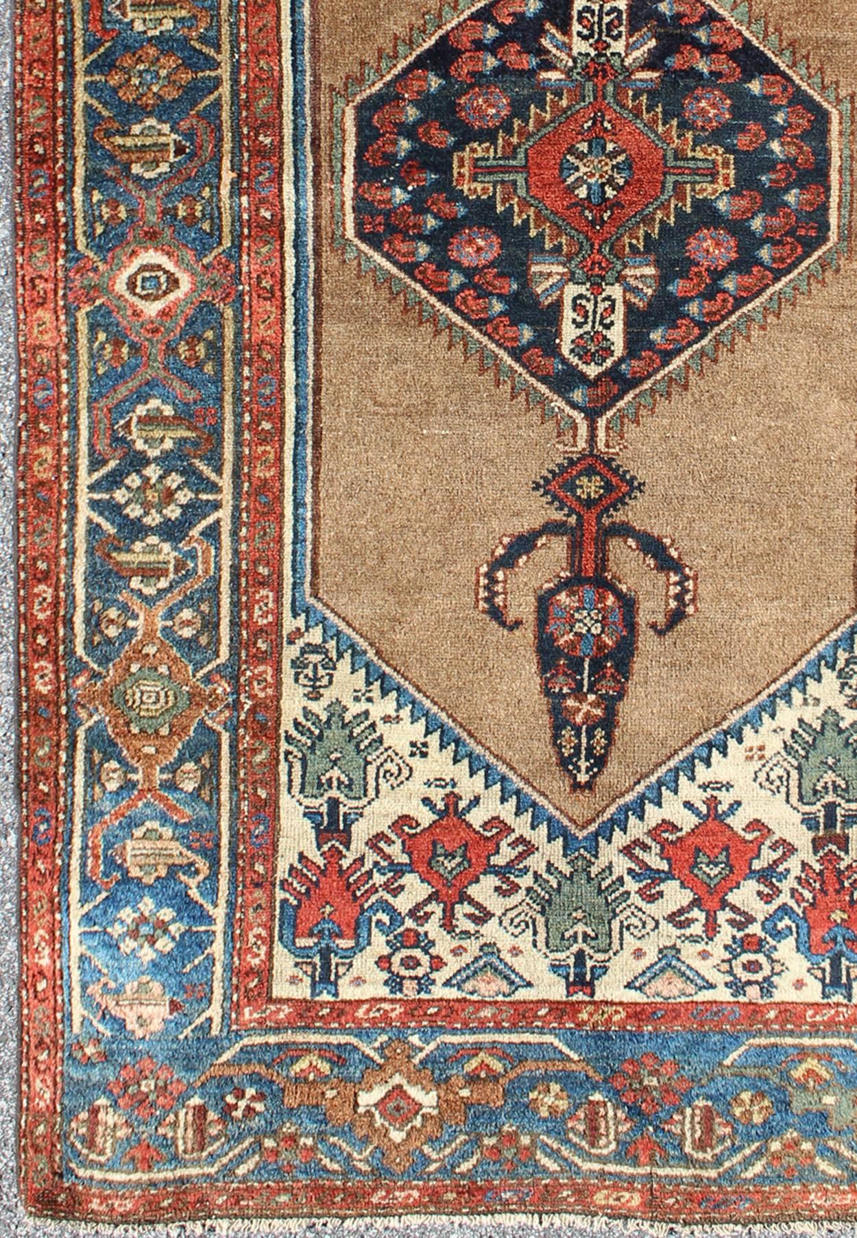 Antique Persian Serab rug with stretched tribal medallion in camel, blue, ivory and red, rug m14-0506, country of origin / type: Iran / Serab, circa 1900

This early 20th century, handwoven antique Persian Serab rug features a camel-colored field