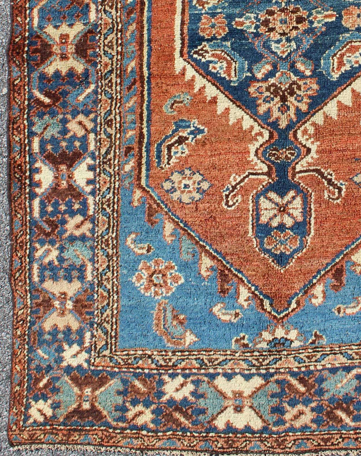 Antique Persian Karadjeh rug with tribal medallion in rust red and bright blue, rugs 12-0104, country of origin / type: Iran / Karadjeh, circa 1910.

This early 20th century, handwoven antique Persian Karadjeh rug features a rust red-colored field