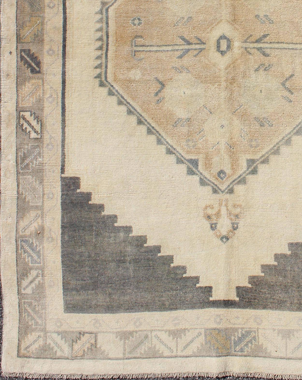 This vintage Turkish Oushak rug features an intricately beautiful design with a tribal aesthetic. The stylized central medallion is surrounded by multi-layers in the central field. The various shades of taupe, charcoal, grey and cream blend