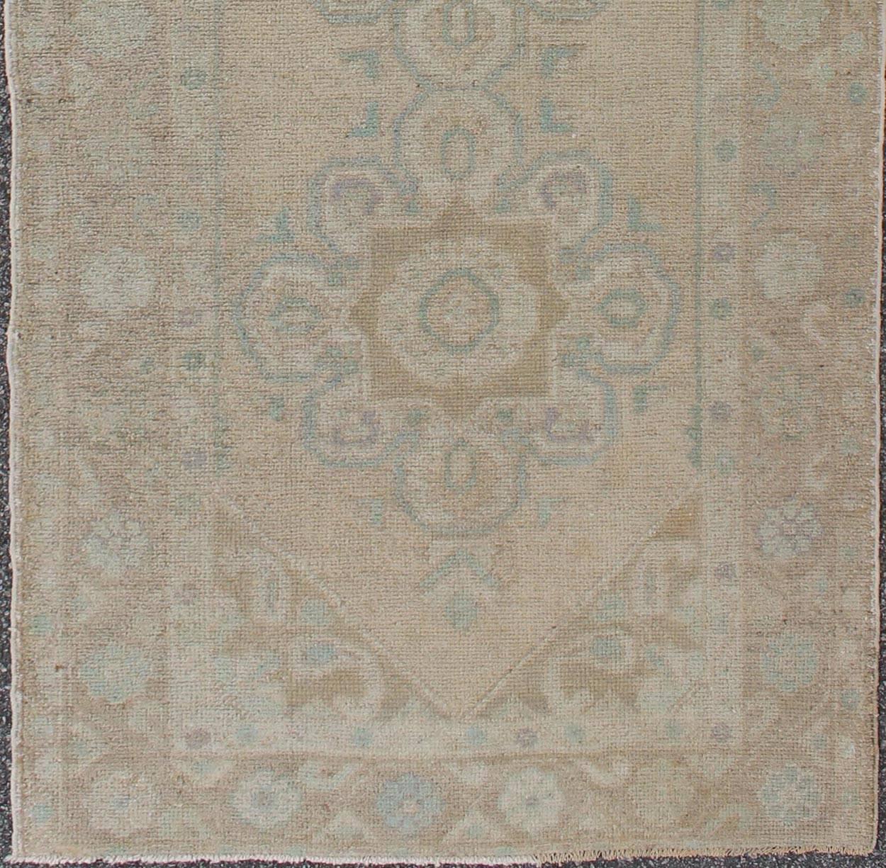 This vintage Turkish Oushak gallery rug (1930) features a unique blend of colors and an intricately beautiful design. The central medallions consist of a vertical line of floral elements, surrounded by a complementary pattern in the border. The