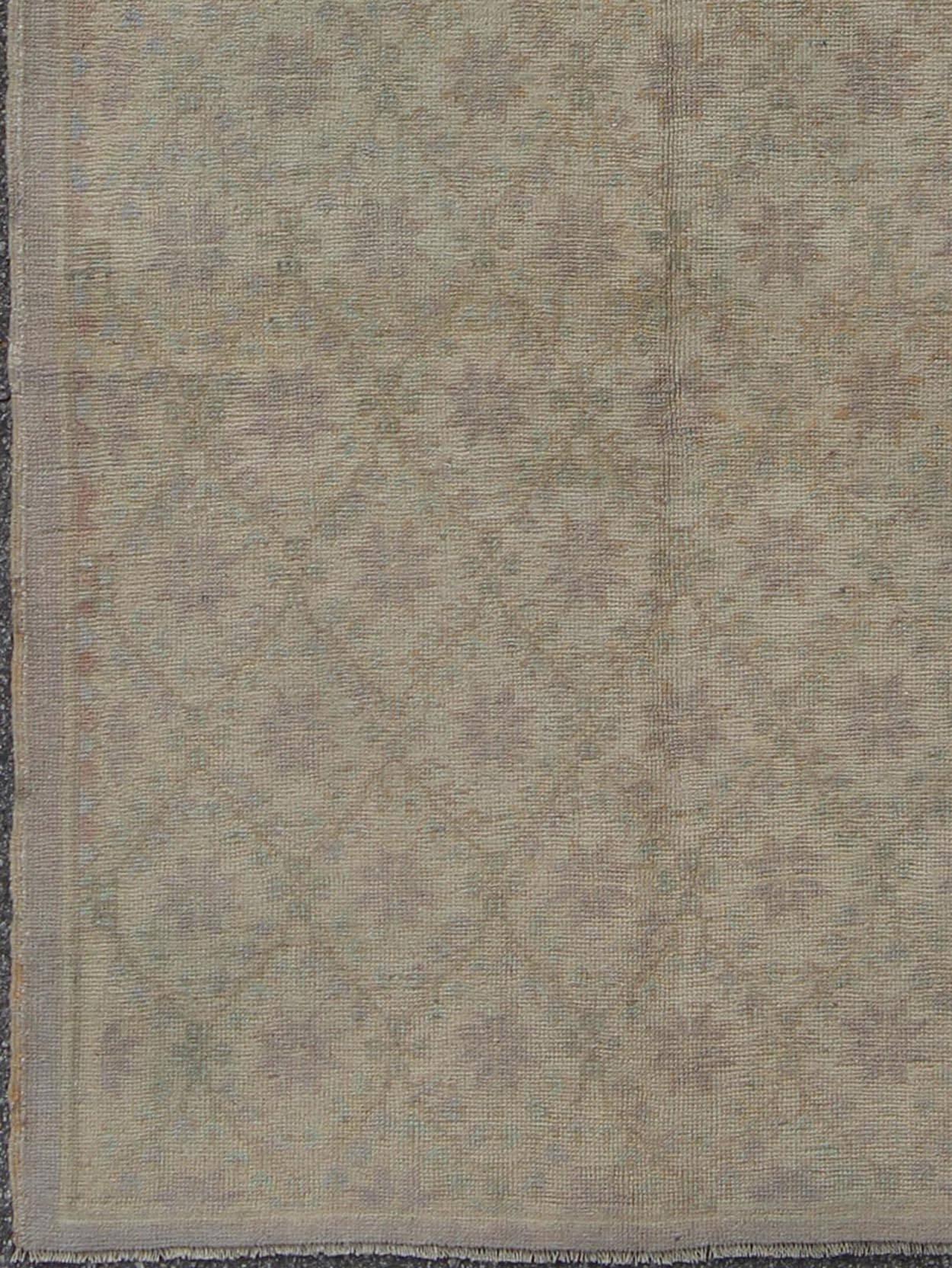 This Oushak carpet (circa mid-20th century) features an all-over pattern of mini blossom-like flowers spreading throughout the central field. Colors include various shades of taupe and gray. The rugs' qualities are enhanced by its lustrous