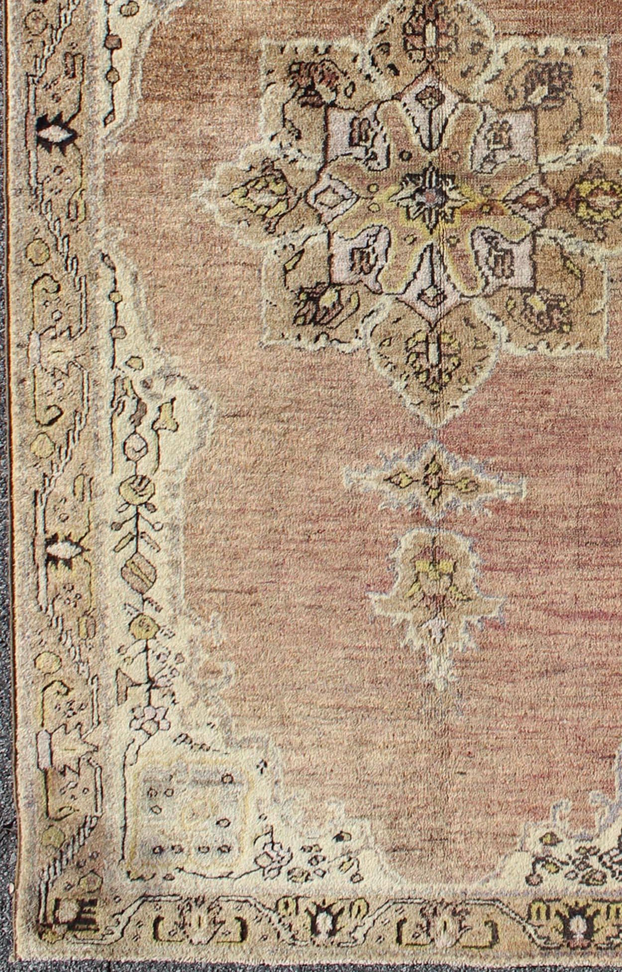 This vintage Turkish Oushak rug features an intricately beautiful design with a stylized floral aesthetic. The central medallion is surrounded by four cornices in the central field. The various shades of cream, yellow, charcoal, and gray blend