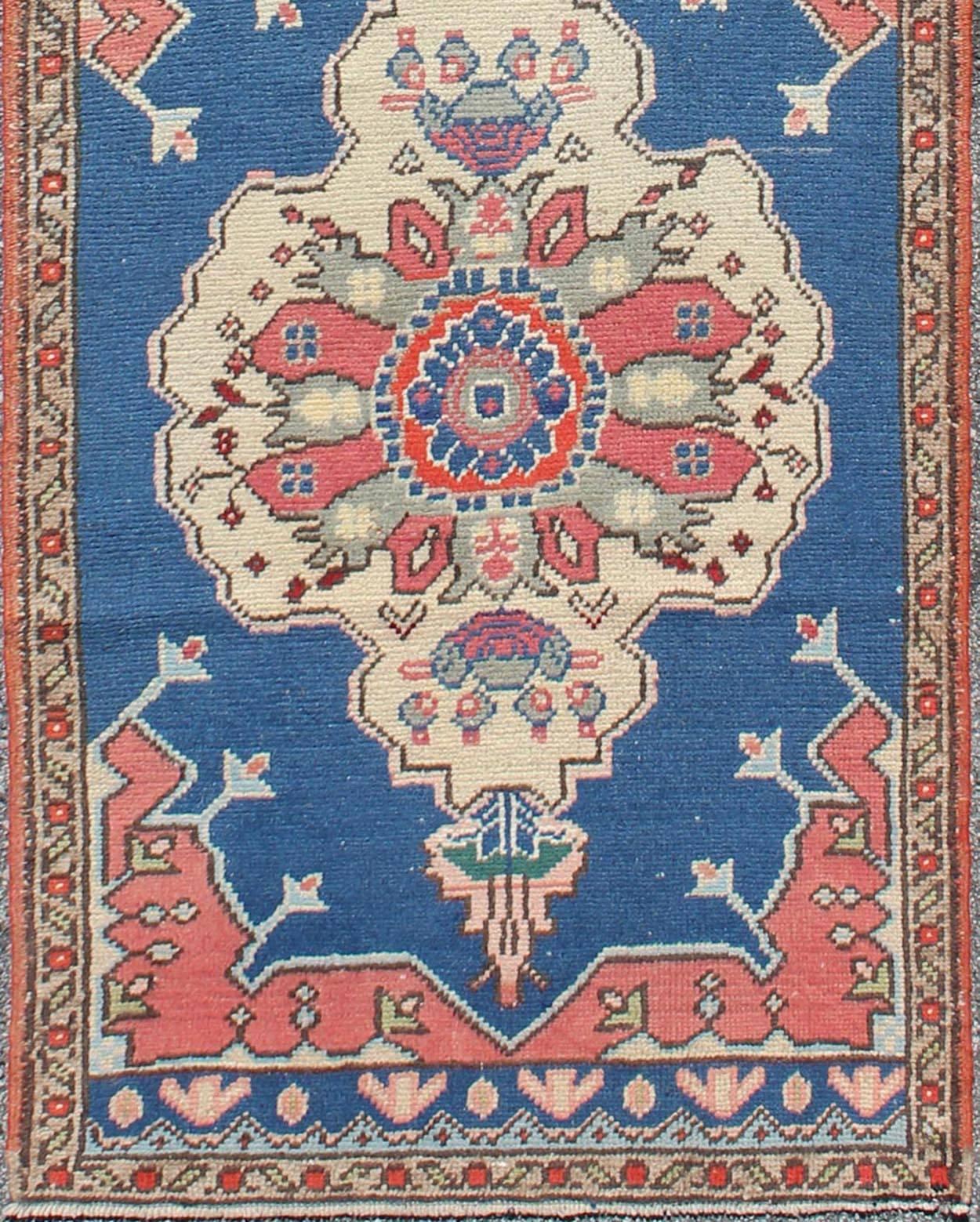 This Turkish runner features a dual central medallion design as well as patterns of smaller geometric and tribal elements. Colors include various shades of red, royal blue, ivory, and gray. Turkish Oushaks are notable for the grand, monumental scale