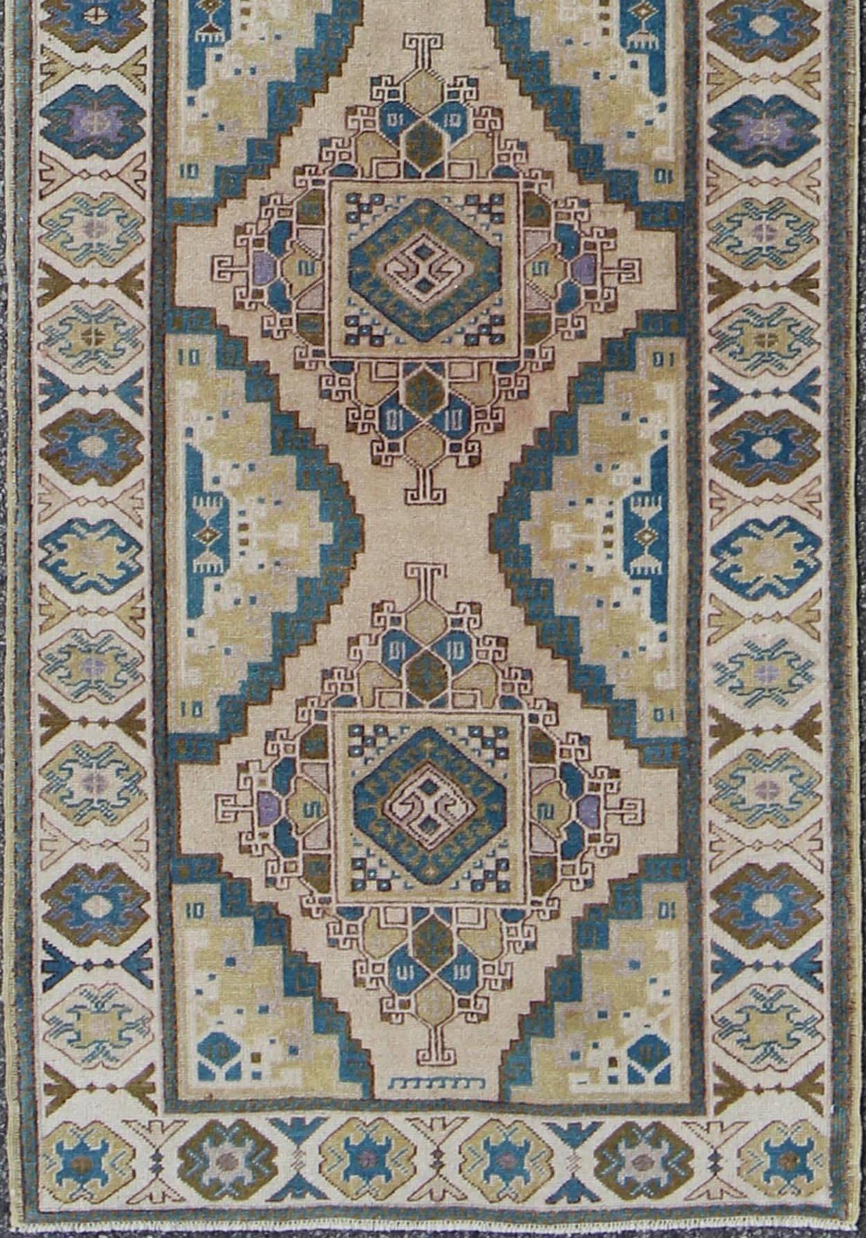 This vintage Turkish Oushak gallery runner (circa 1930) features a unique blend of colors and an intricately beautiful design. The central field is adorned with a plethora of vibrant sub-geometric shapes, which are surrounded by complementary