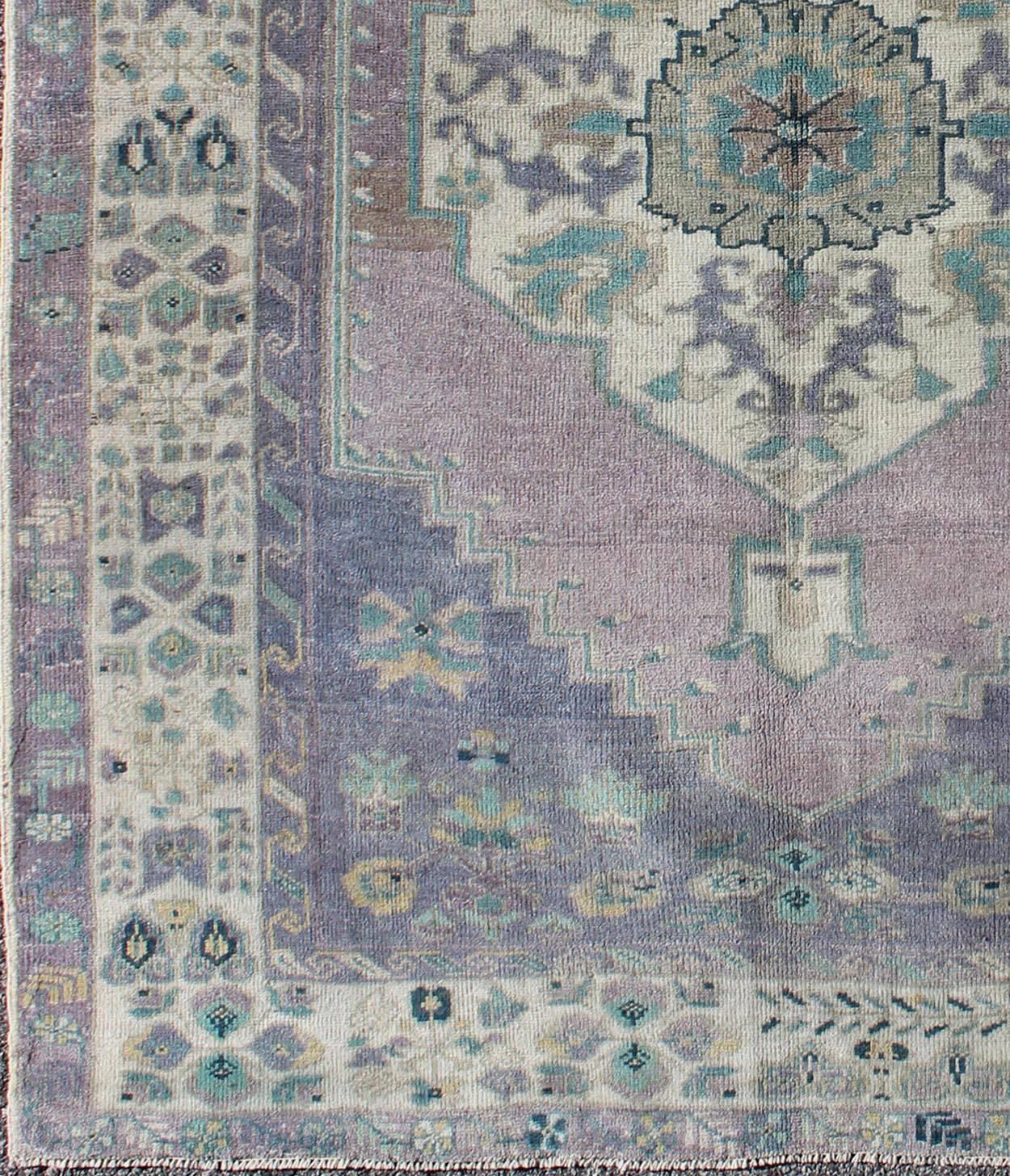This vintage Turkish Oushak rug features an intricately beautiful design with a floral aesthetic. The central medallion is surrounded by multi-layers in the central field. The various shades of lavender, teal, gray, and cream blend beautifully with