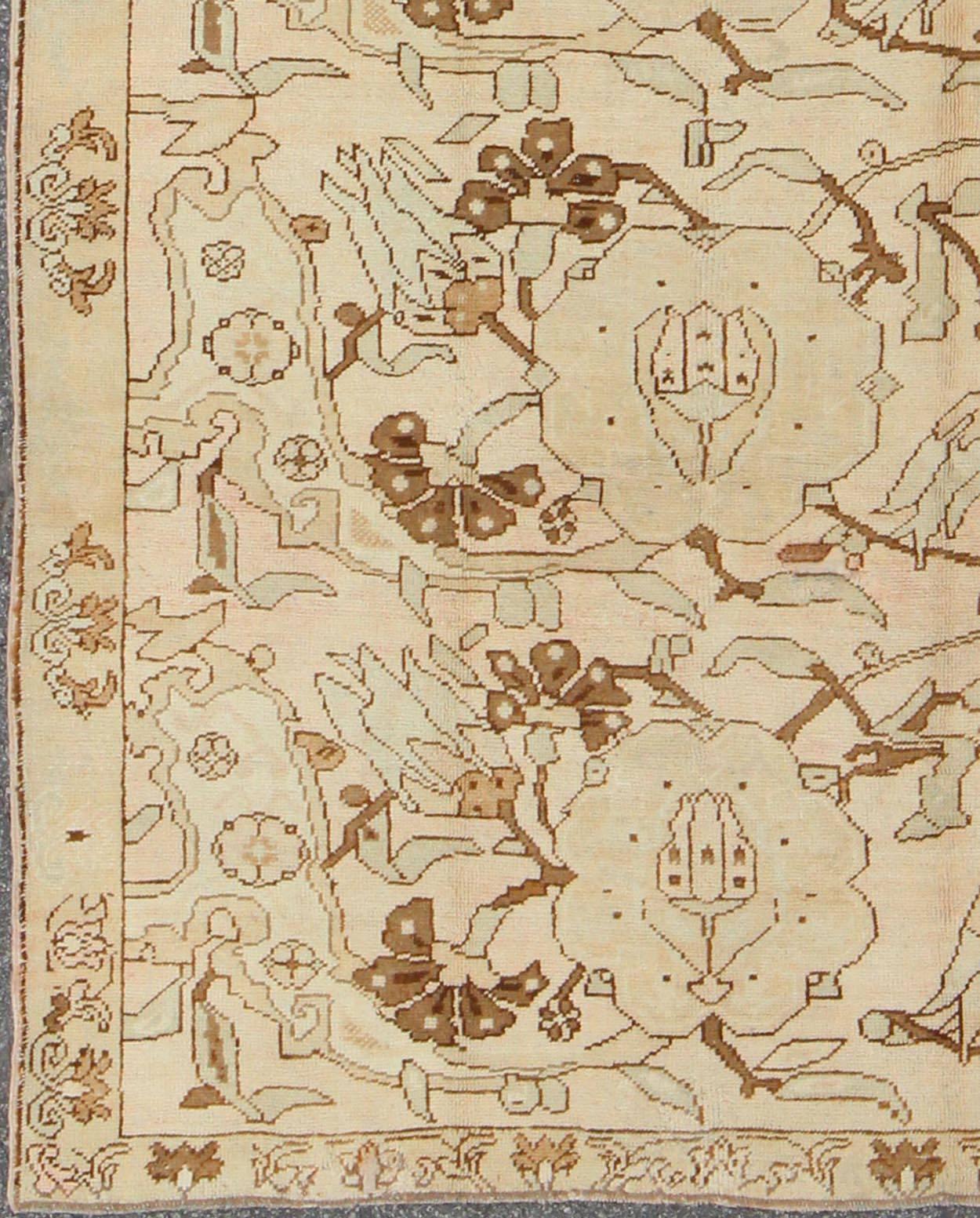 Sur un fond aéré de couleur crème, ce magnifique tapis Oushak turc du milieu du siècle dernier (vers 1940) présente des motifs de fleurs répétitifs de couleur marron, taupe et crème flottant sur le champ. Une simple bordure au motif complémentaire