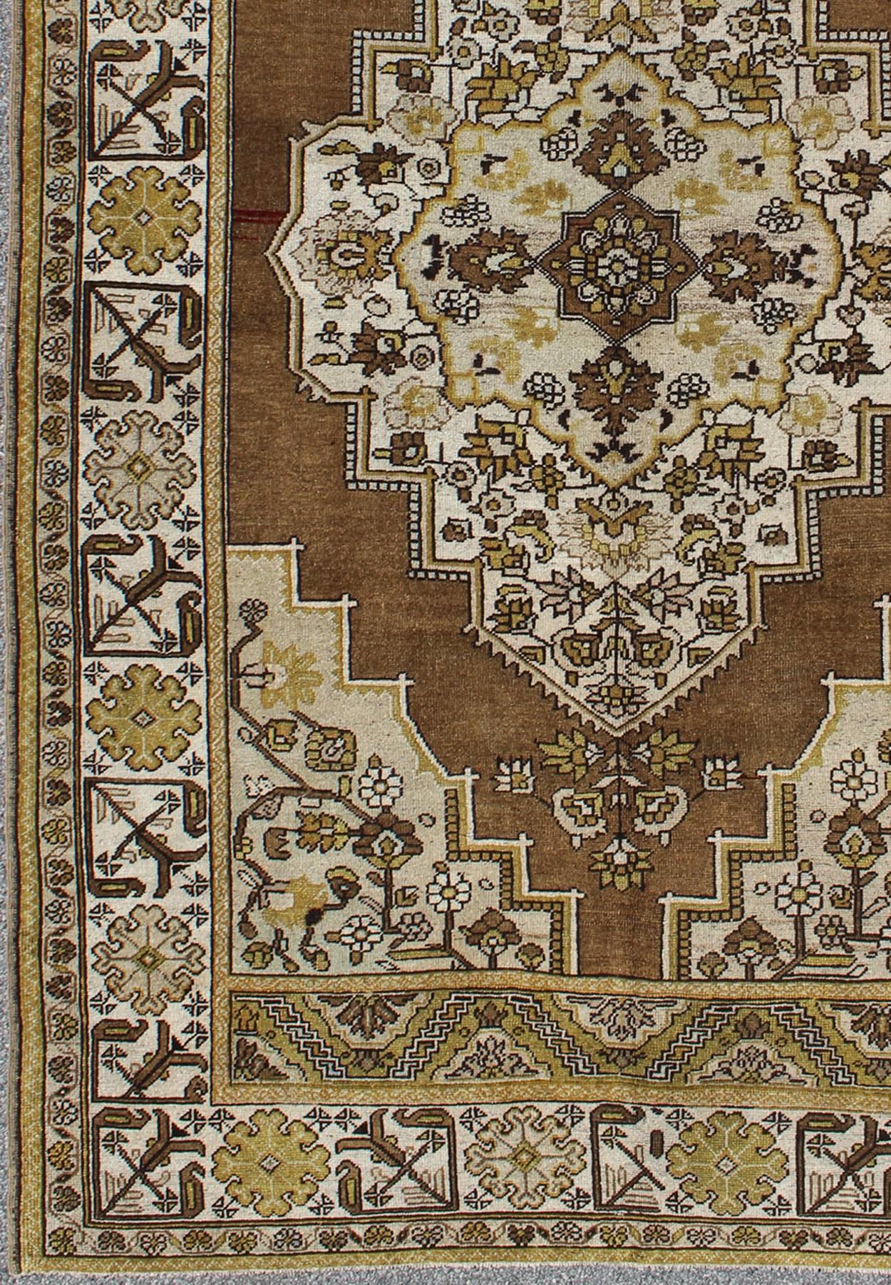 Measures: 6'4 x 9'11.
This vintage, midcentury Turkish Oushak rug features an intricately beautiful design with a floral aesthetic. The central medallion is surrounded by multi-layers in the central field. The various shades of mocha brown and