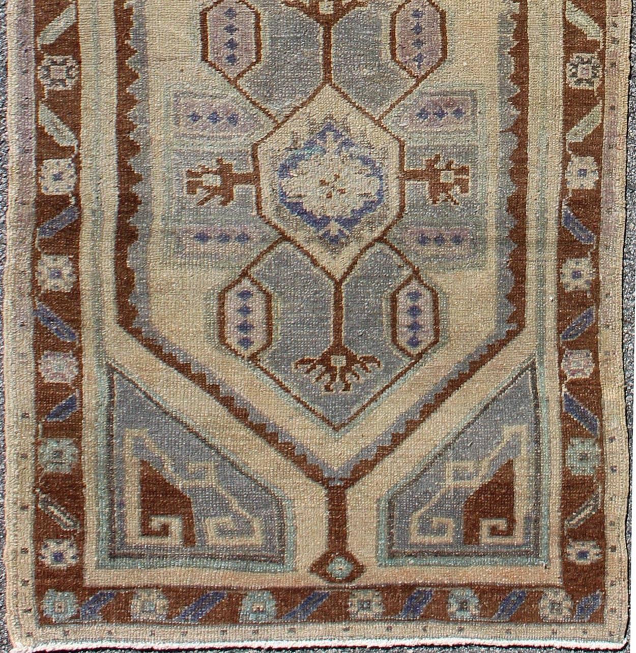 This vintage Turkish Oushak carpet (circa mid-20th century) features a tribal, central dual-medallion design, as well as patterns of geometric elements in the surrounding field and borders. The rug's qualities are enhanced by its particularly soft