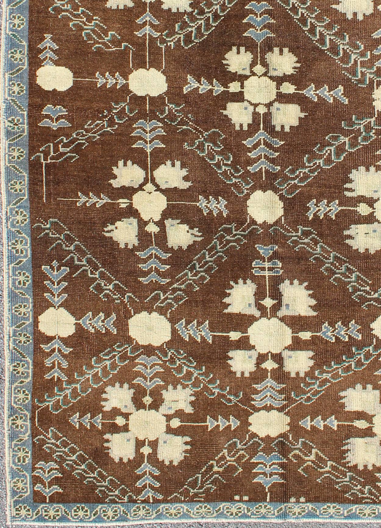 This piece features a stunning chocolate background with an all-over pattern in blue and ivory with hints of green. The blue border has a small repeating flower design. 
Measures: 5' x 9'4