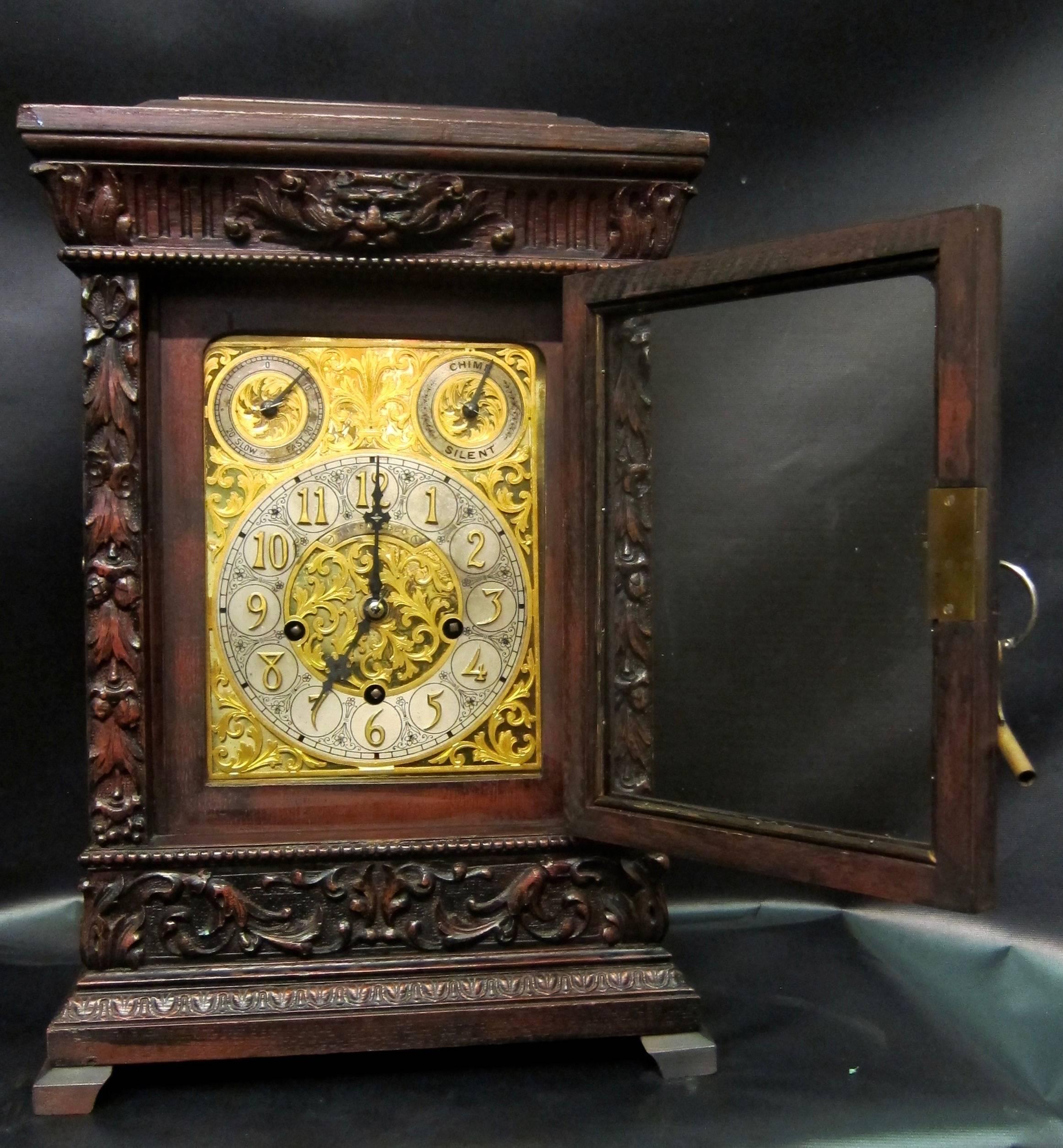 This early 20th century Tiffany & Co. mantel clock is designed in a decorative solid dark oak case. This clock case has beautifully carved accents, including one of the North wind diety above the front door. Behind this key lock hinged glass door,