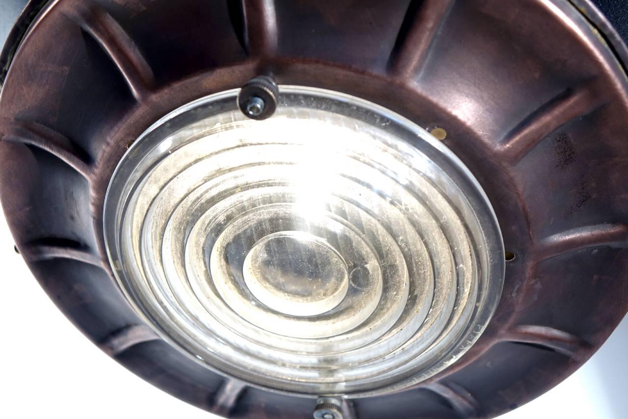 This large spun metal spot has an 18 inch diameter and is 22 inches tall. The inside has a mirrored finish the lens is a prismatic bullseye and the lamp is set up to hang as a large dramatic pendant. The finish is stove black with top and bottom
