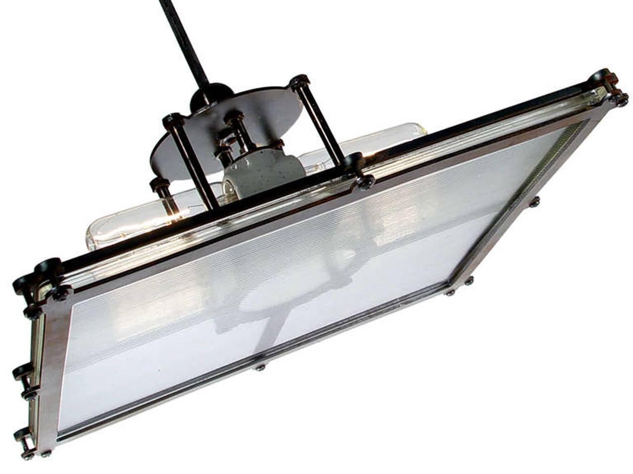 This oversized pendant features a substantial 15"x 17" prismatic glass plate. The prismatic design casts a beautiful 3D glow. The lamp has a heavy blackened brass and steel frame and is lit buy four floating horizontal tubular bulbs using
