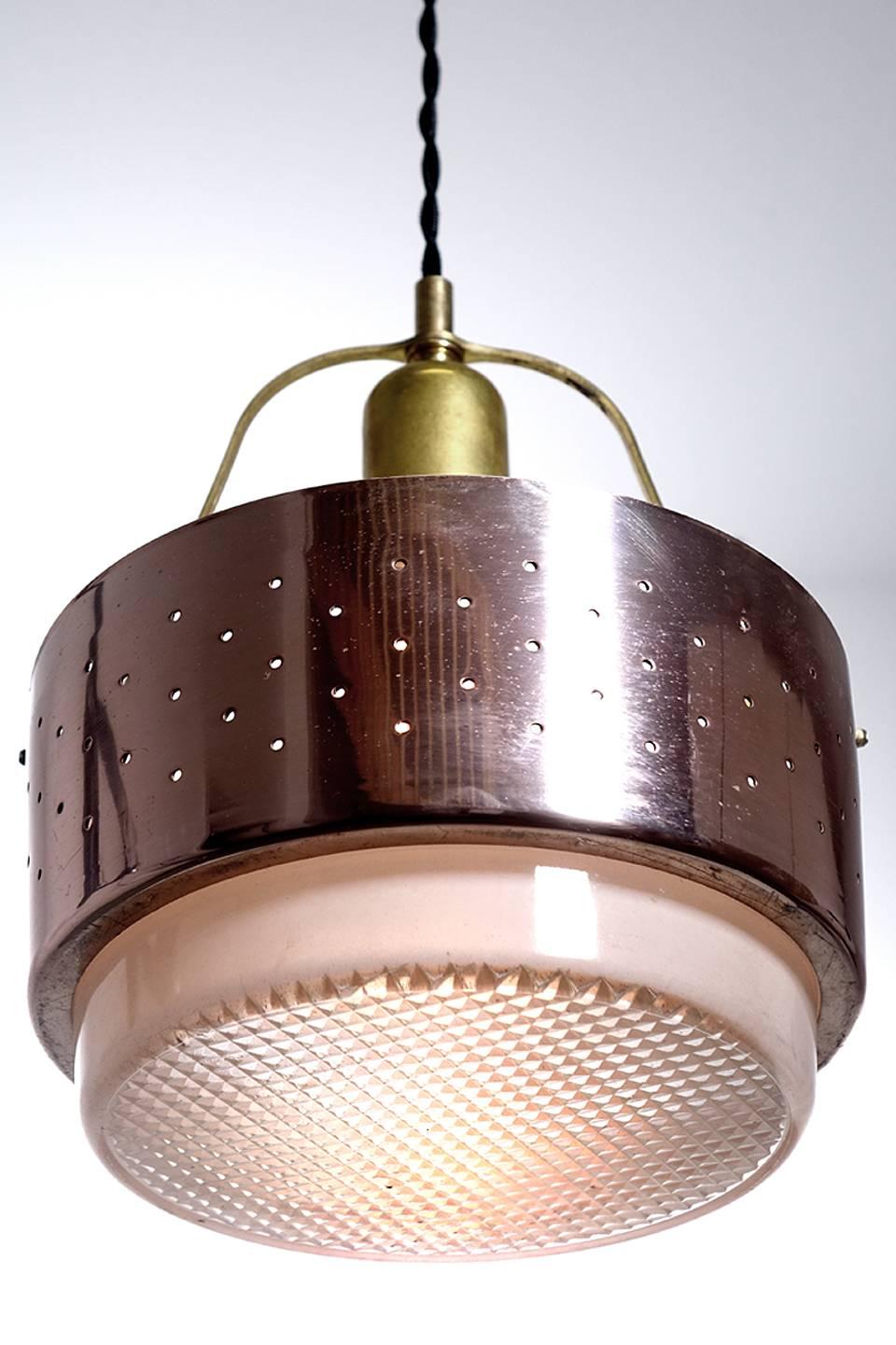 We have a collection of these unique simple Mid-Century Modern lamps. It consists of a perforated copper ring with a thick waffle pattern glass lens. It hangs from a brass bow and center socket. There is a nice open look to the whole design and they