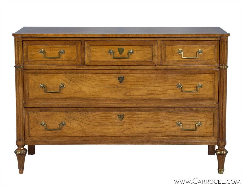 This charming chest is constructed with rich distressed walnut and designed in the Georgian style. It has three equal sized drawers with recessed panels, brass escutcheons and hardware. Fluted columns descend down flanking the sides, framing the