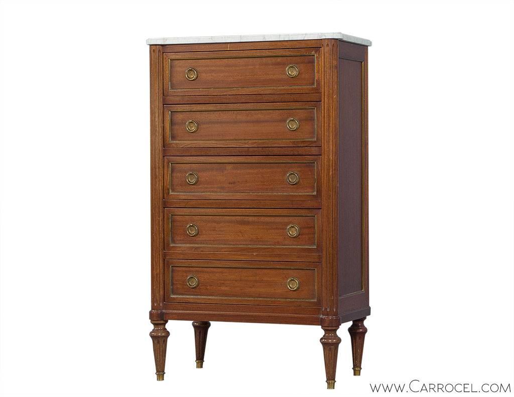 A gorgeous chest of drawers made of walnut wood in the Louis XVI style, circa 1900s. The commode features five drawers with trim in brass and classic laurel wreath brass handles. The sides are fluted and the legs tapered. The removable marble top is