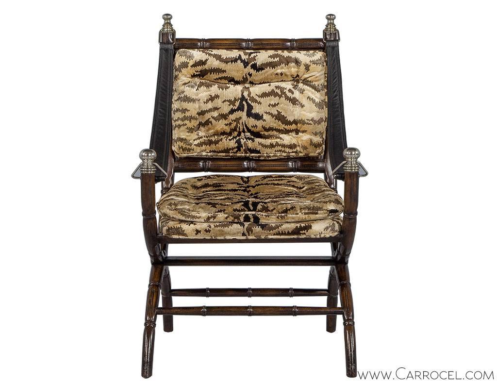 A vintage Hollywood Regency curule accent chair, with a faux bamboo frame, cane back, chrome capped arm ends and newly replaced leather arm straps. The zebra pattern upholstery on the seat and back bring a touch of glamour to the chair and