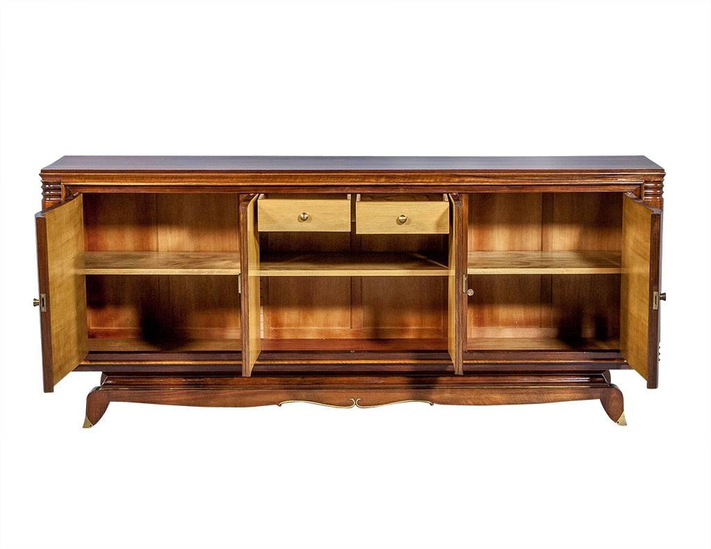 Stunning deco buffet attributed to Jules Leleu designed with contrasting burled wood doors inlaid with ‘X’ motifs in satinwood, fluted details wrapping around the sides, as well as brass accents and hardware. The central compartment is outfitted