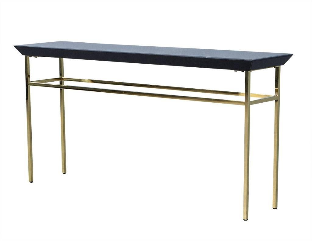 Sleek console table made of thick, tempered and black glass. The glass tabletop is supported by gold finished stainless steel legs with an extra gold wraparound underneath the base. A Minimalist, chic piece that would bring timeless class and style
