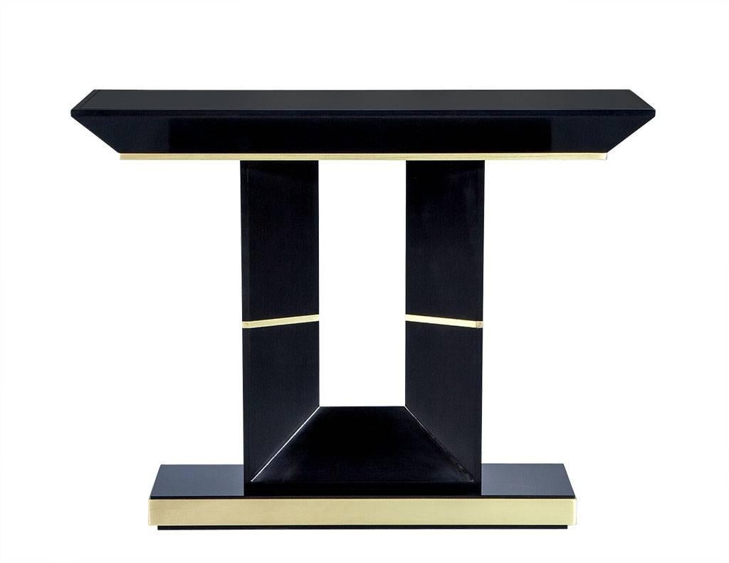 Custom-made by Carrocel Art Deco console hall table. Finished in hand polished black lacquer accented with brass trim under the apron, surrounding the base and through the pedestal. Topped with a black back painted glass top.