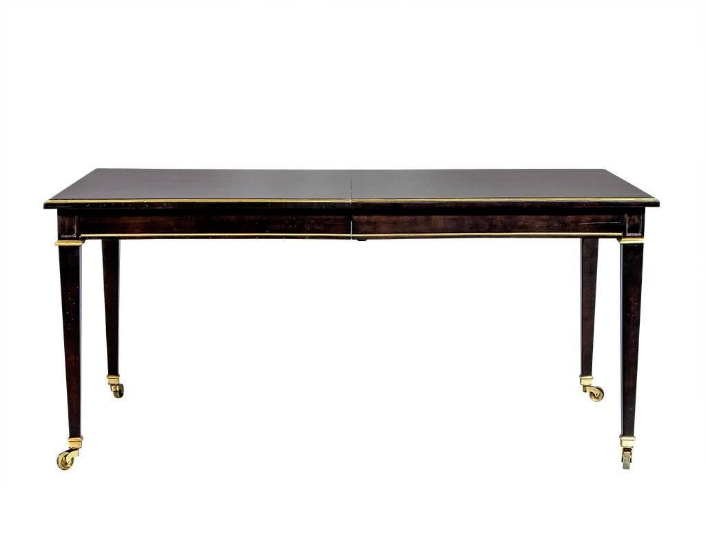 Clean lined transitional walnut dining table, newly restored in dark espresso finish. Has satin gold trim around the table top, apron and foot caps. The table is on caster and extends to 102” roughly 8.5ft with two accompanying leaves installed.